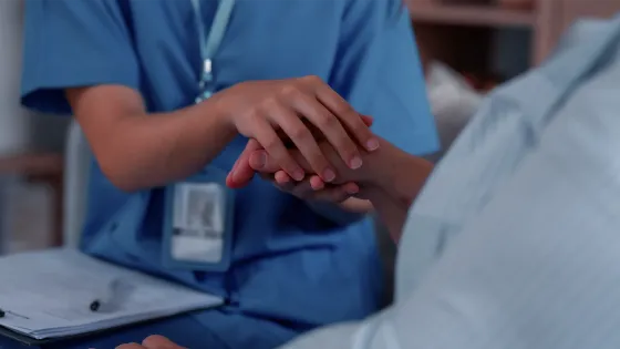 A home care nurse in blue scrubs holding hands with an elderly patient, offering support and comfort in a home setting